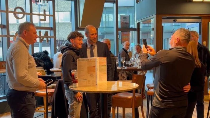 Side angle photo of Prince William posing for a picture with a football fan