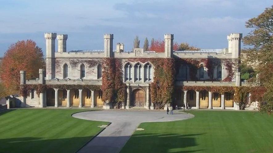 Historic ivy-covered grey court building in the grounds of Lincoln Castle, with a path and lawned area in the foreground