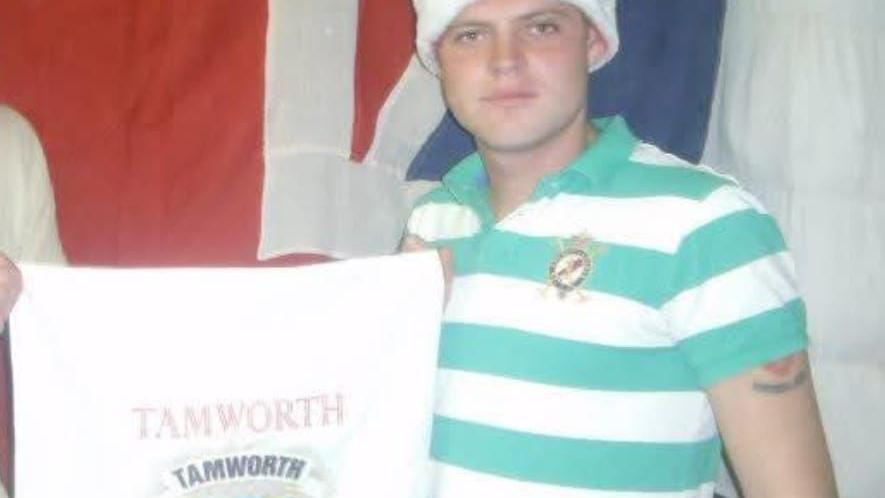 A young Scott Farrington holding a Tamworth cloth. He is wearing a white and blue polo shirt and has a hat on. Half of his Tamworth FC tattoo can be seen. 