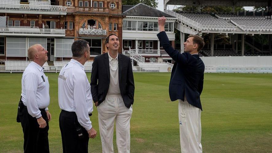 Two umpires and a player watching a player toss coin