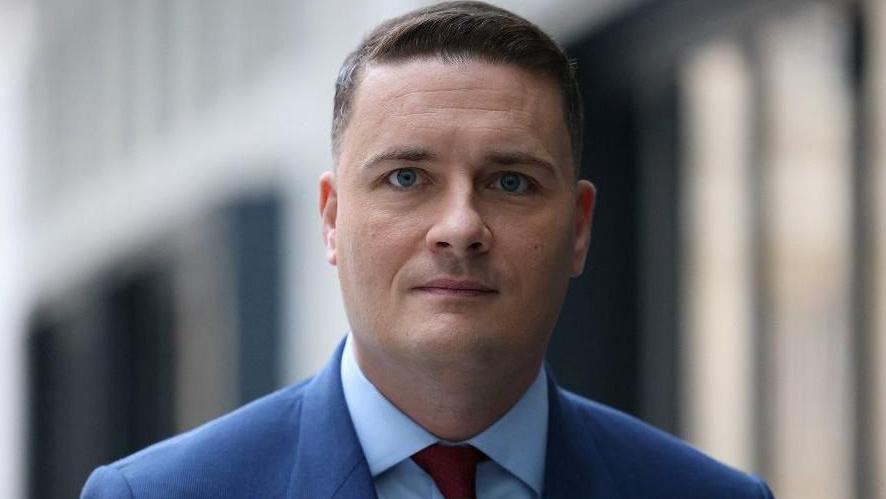 Wes Streeting standing in front of a building, looking directly into camera