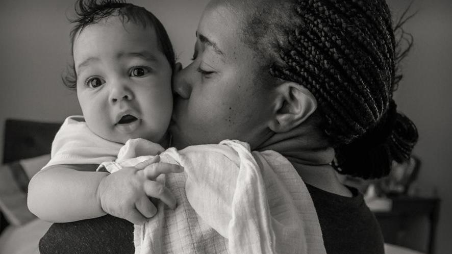 Shalom and Joshua Lloyd, a woman holding a baby, the picture is in black and white and the woman is kissing the boy, he is looking at the camera and the woman is looking at the baby