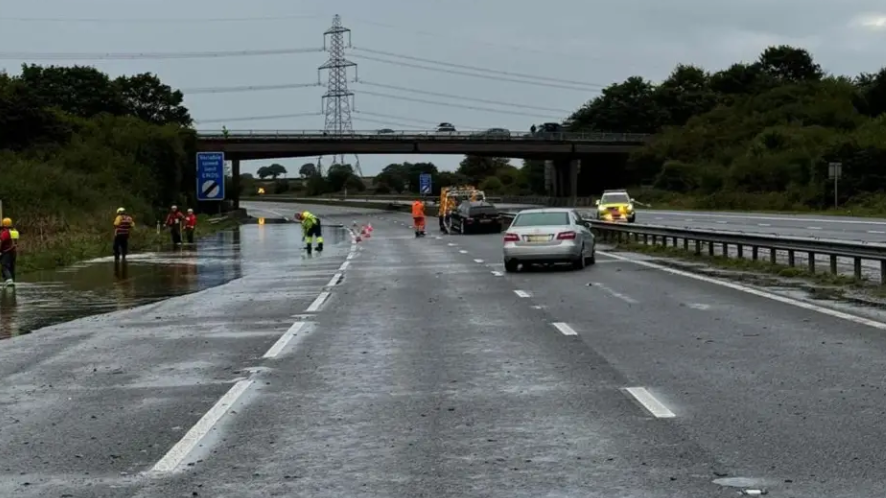 The M5 with an abandoned car and significant flooding on the hardshoulder, with fire and rescue crews dealing with the incident