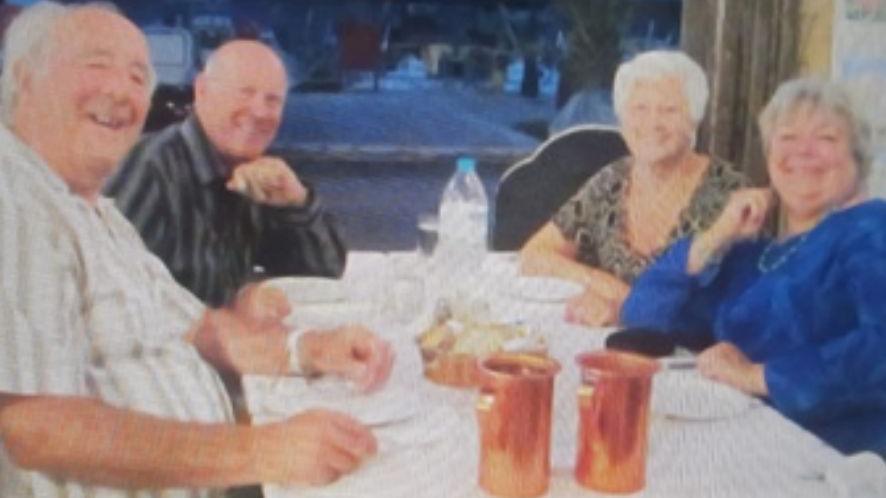 a group of four older people - two men and two women - sit around a table. They are smiling and posing for the camera.