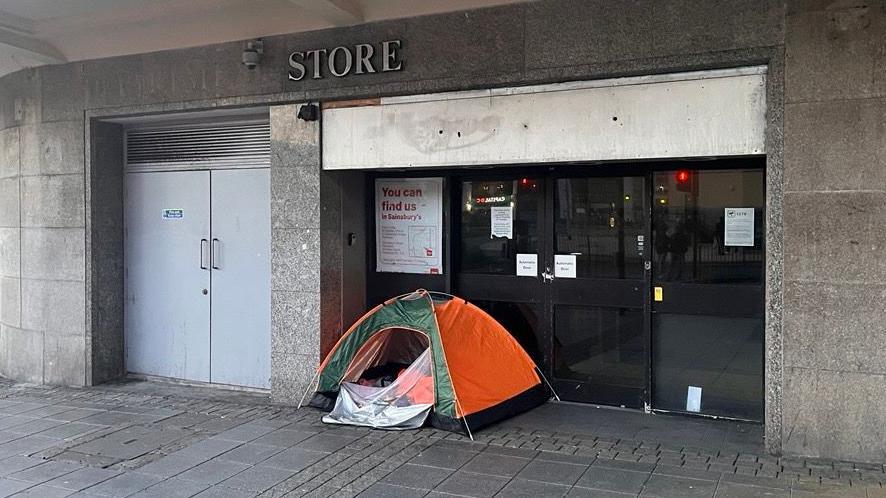 A green and orange tent in the doorway of an abandoned shop.