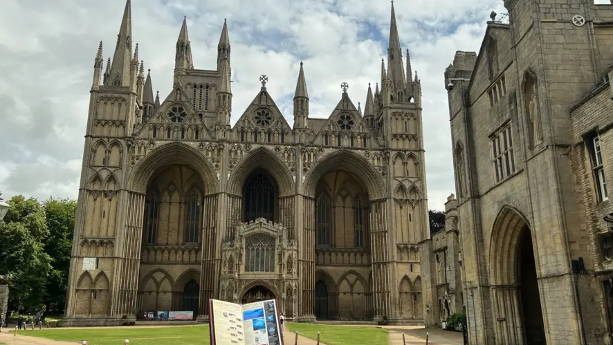 exterior of Peterborough Cathedral showing its spires and a lawn at the front
