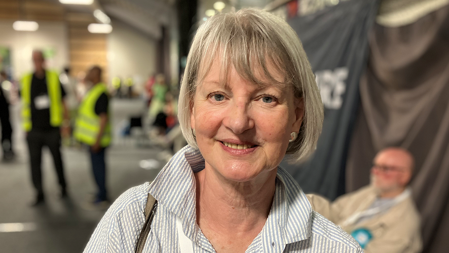 Liz Leffman, wearing a grey and white shirt with the collar turned up, smiling for the camera.