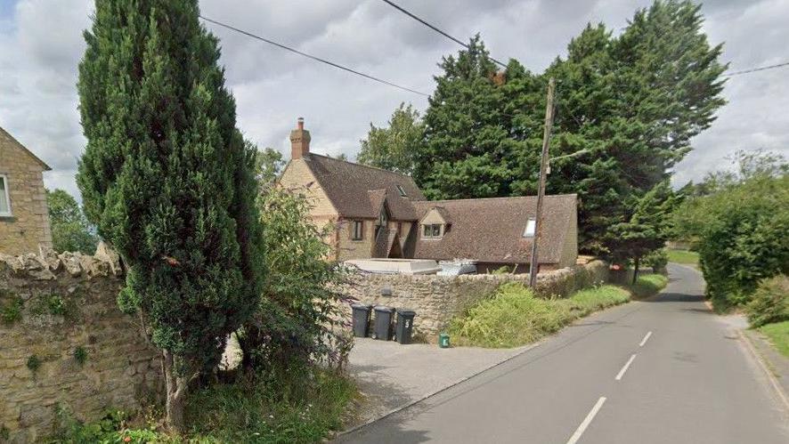 Part of Oxford Road in Garsington, showing a tree-lined road with detached properties surrounded by traditional brick walls