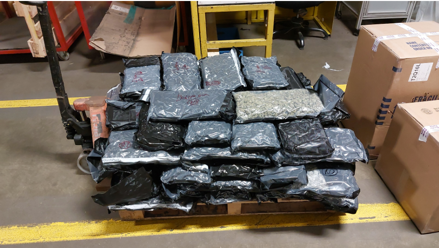Stacks of vacuum-sealed rectangular packs of cannabis seized by police rest on a loading trolley in a warehouse.