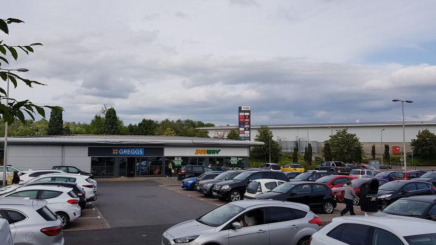 Cars parked in a retail park with Greggs and Subway seen in the background.