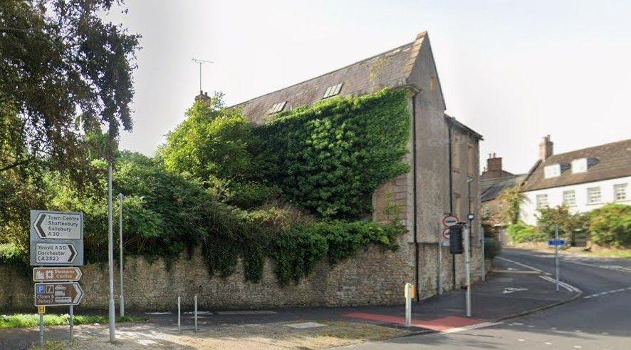 The grey building on a road corner, with ivy growing on the full front and on to part of the roof