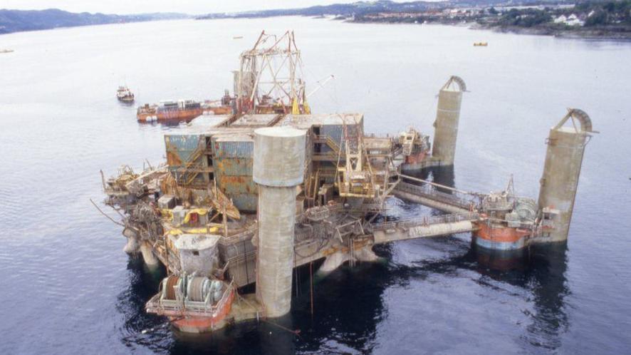 Aerial view of the platform after it s has been turned back over. There is a tower of cargo container's on the deck and the remains of three large metal legs on the sides