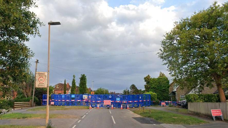 The road closure in Kidmore Road, Caversham as seen in May 2025. There are multiple blue road barriers around it.