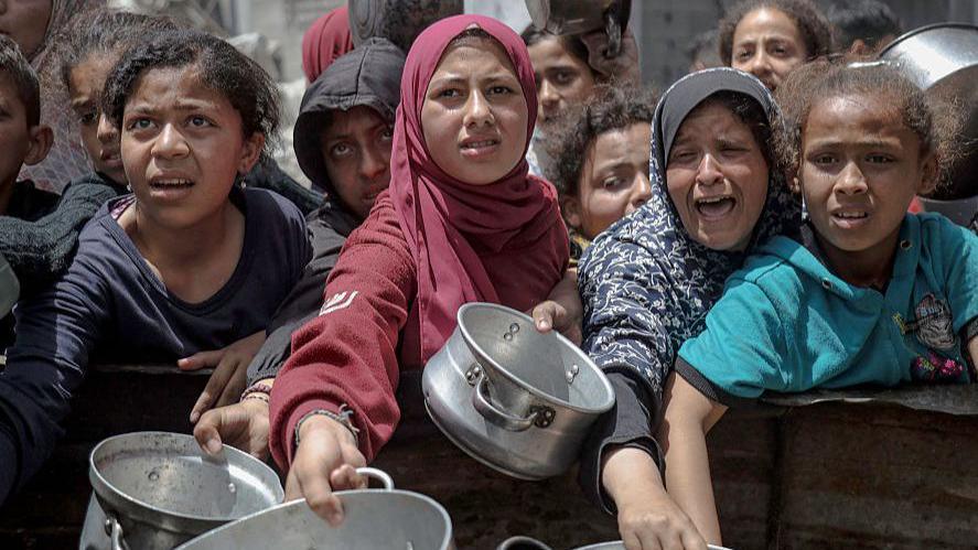 Women and children extend their arms with empty pots to collect food in a refugee camp in Gaza City this week.
