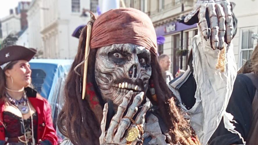 A person posing for the camera wearing a skeleton mask and pirate headband with dreadlocked hair