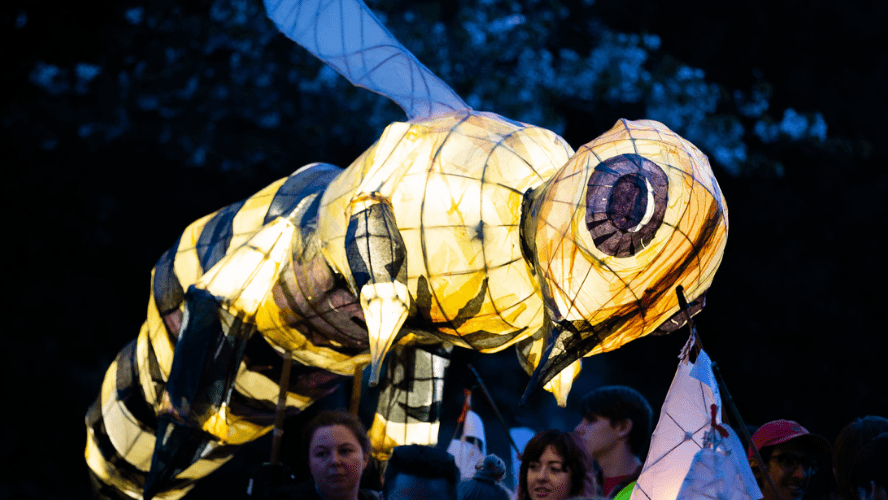 A large paper lantern in the shape of a bee being carried by two women