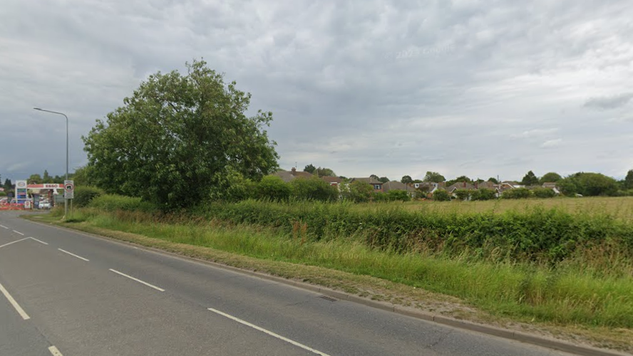 A Google Street View image of the land, which has a road running past a field and existing homes in the background.