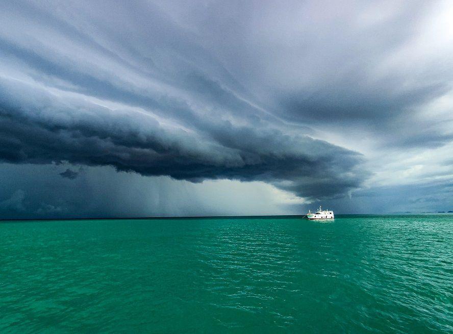 A boat sits on flat turquoise water as a dark thunder cloud is seen coming in from above 