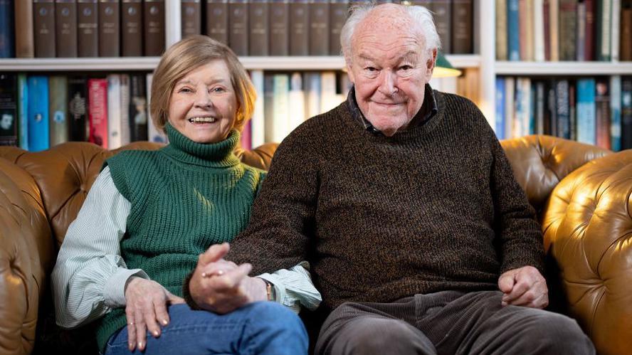 Prunella Scales and Timothy West pictured sitting on a sofa with a book shelf behind them