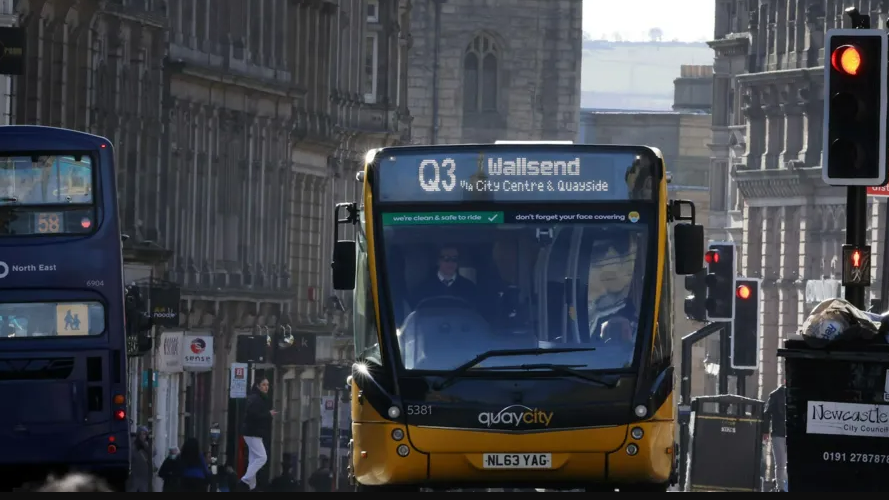 A yellow bus with a Q3 sign climbs up a hill in Newcastle City Centre.