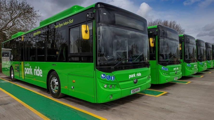 A row of green Leicester park and ride buses side by side in parking bays with green and yellow markings.