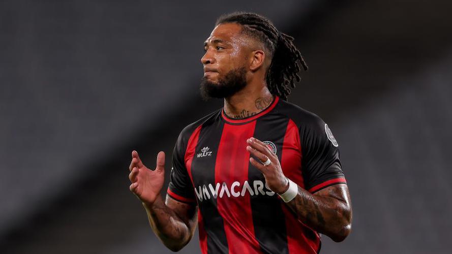 Crawley Town manager Colin Kazim-Richards in his plaing days wearing black and red vertical stripes of turkish side Fatih Karagumruk SK, holding hands up in front of his chest about to clap