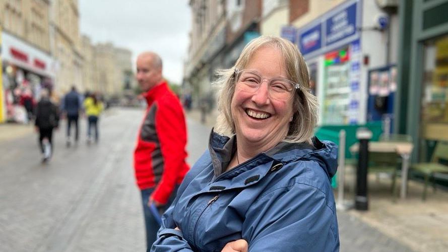 Simone Pengrave, a white woman who's wearing thick-rimmed clear glasses and a blue waterproof coat