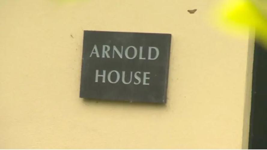 A yellow wall with a black slate sign hanging that reads 'Arnold House'