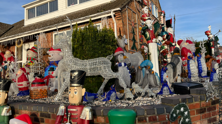 It is daytime. Part of the house is covered in lights and Christmas decorations. There are snowmen models as well as soldiers, Santa Claus models and penguins.