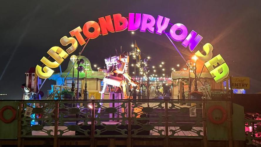 A multi-coloured sign in the darkness says Glastonbury on Sea.