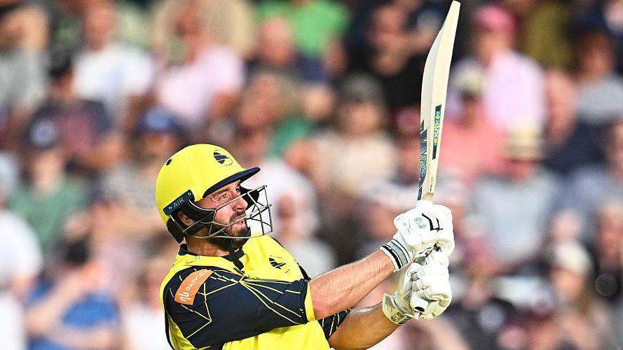 James Vince, wearing a yellow shirt, helmet and white gloves, plays a shot with his bat