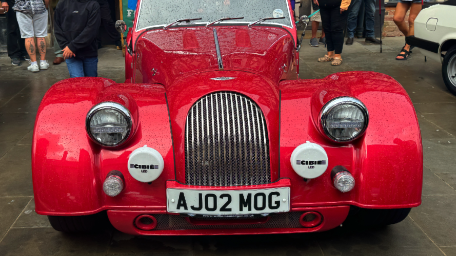 A bright red car, 2002 plate, but in the style of a vintage sports car, appears to have a Bentley badge