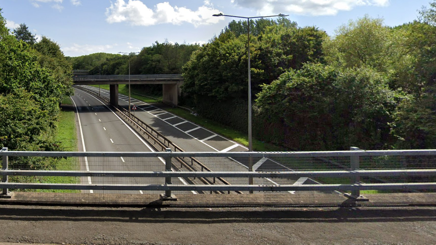 A view of the A442 carriageway from a bridge at Wombridge. The road is clear in both directions with trees either side of it.