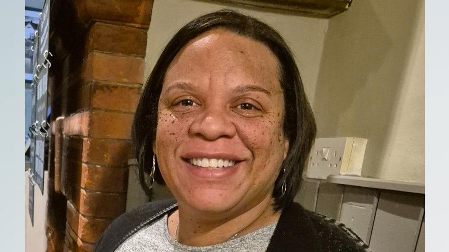 Danielle Parrott is looking towards the camera smiling. She has short brown hair and is wearing a light grey T-shirt with a dark grey cardigan.
