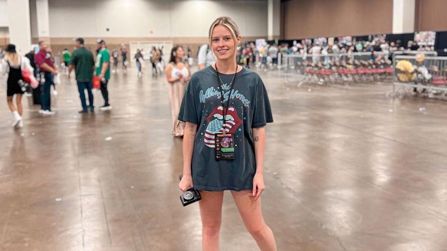 Chloe s wearing an oversized Rolling Stones t-shirt and stood on a large convention floor.