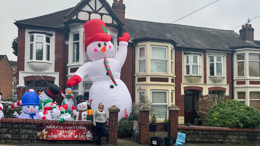 A row of houses with an enormous blow-up snowman outside one of them, almost to the roof, and half a dozen or so smaller ones, all in the front garden, with a woman standing by the gate post