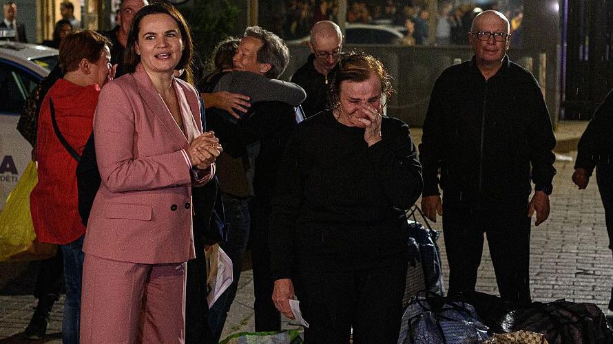 A woman wearing a pink suit greets prisoners in tears as they arrive in the dark in Lithuania