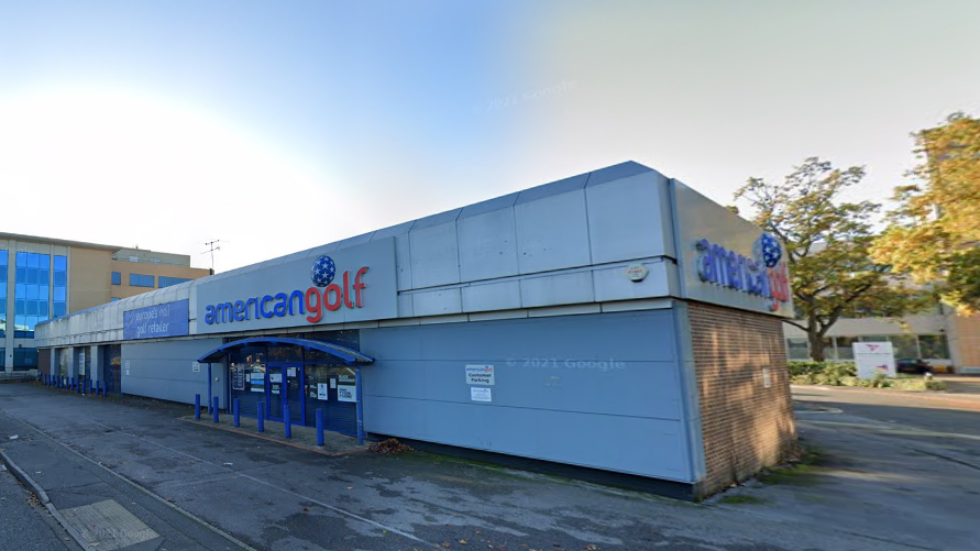 A single-storey building, with a tarmacked entrance, with signs on the front and on the right side of the building that say, in lower case lettering "american golf"