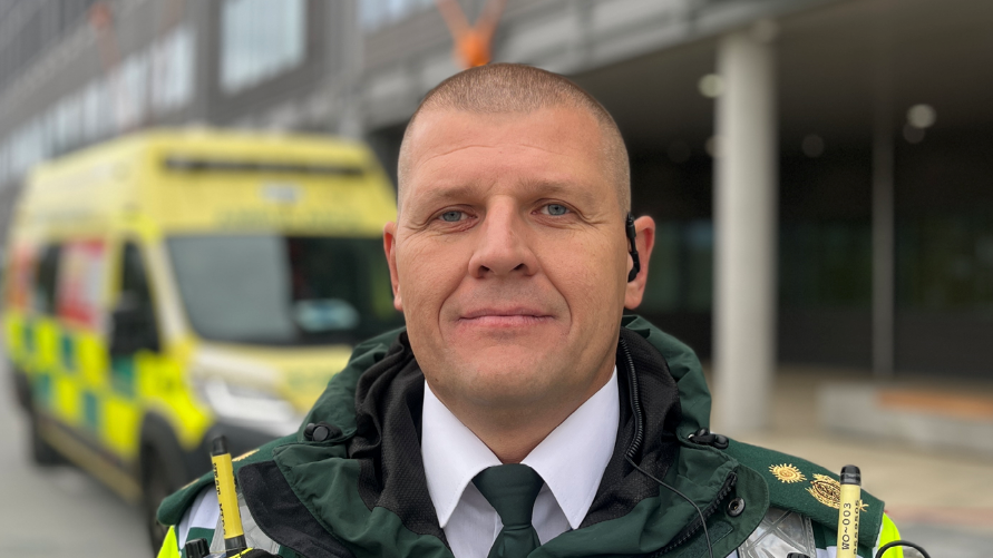 WMAS head of emergency preparedness, resilience and response, James Williams wearing a paramedics uniform stood in front of a blurred ambulance 