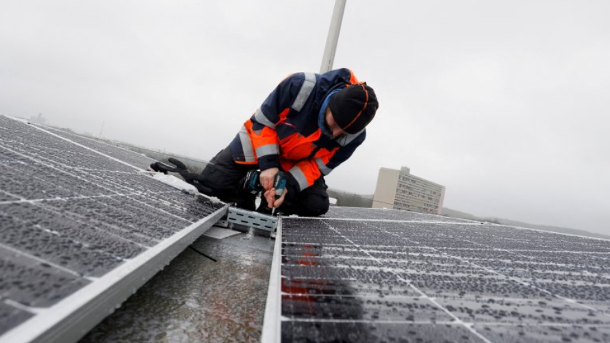 A man wearing a high-vis jacket, fitting solar panels on a roof in the rain.