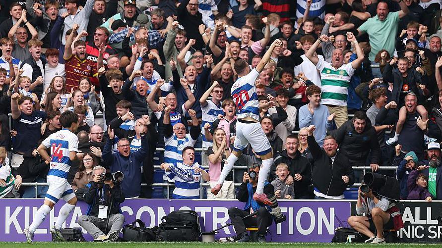 QPR player Harvey Vale leaps into the air in front of celebrating fans after scoring against Stoke City