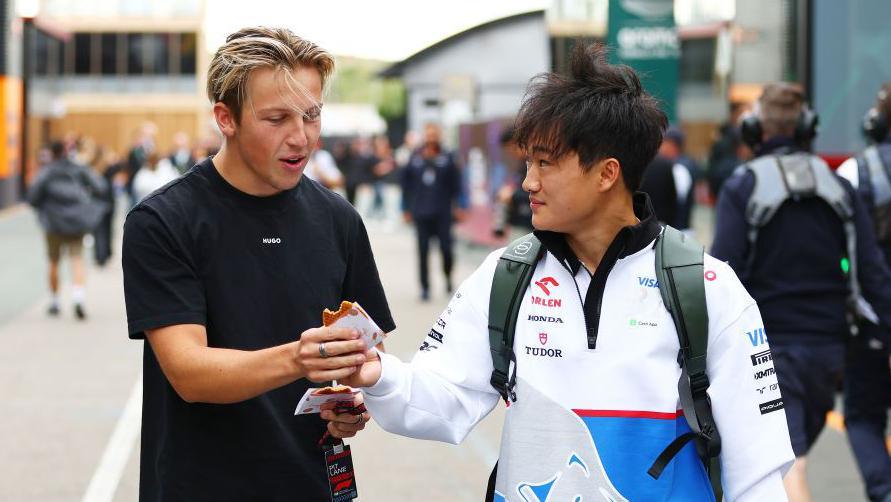 Liam Lawson and Yuki Tsunoda walking in the paddock while carrying some food