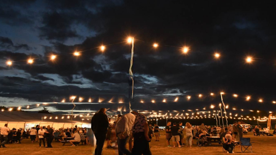 Fairy lights alongside a marquee with people on benches drinking beer