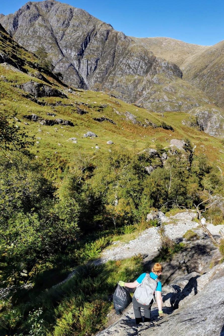 A ranger carrying a bin bag negotiates a large rock in Glen Coe