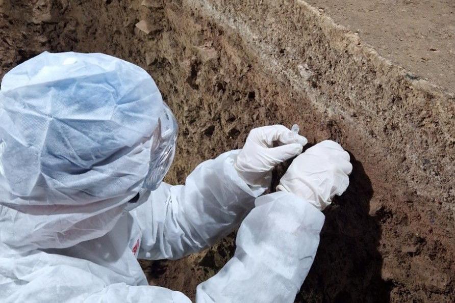 Archeolegydd mewn siwt wen yn cloddio ar y safle