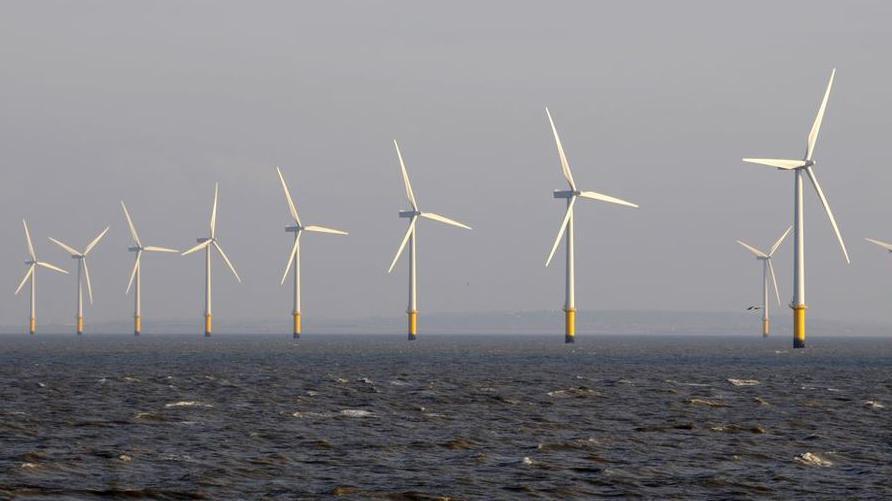 A line of wind turbines in the sea. The blades and tower are white with yellow at the base 