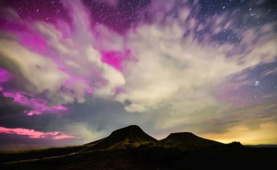 The northern lights in Bannau Brycheiniog National Park with clouds and stars in the sky, with the dark figure of a mountain underneath the sky 