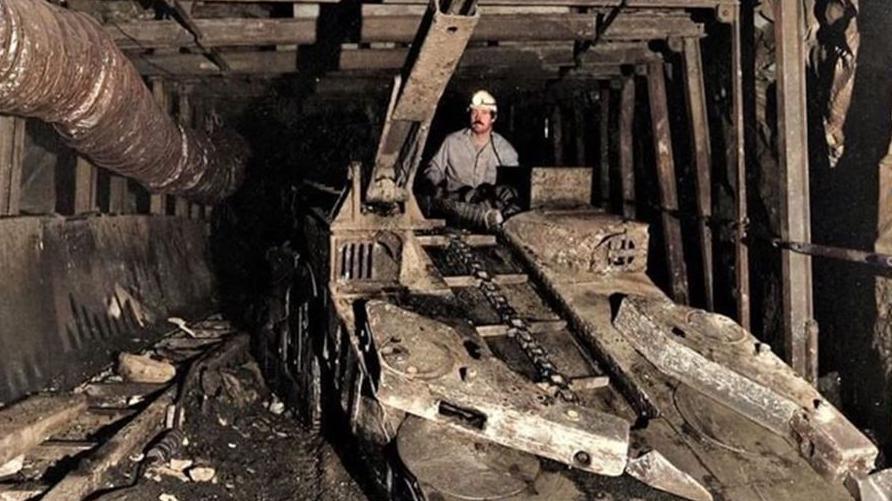 Stuart underground at Woodhorn Colliery, wearing a miner's helmet with a light attached on top of mining equipment used down the pits.