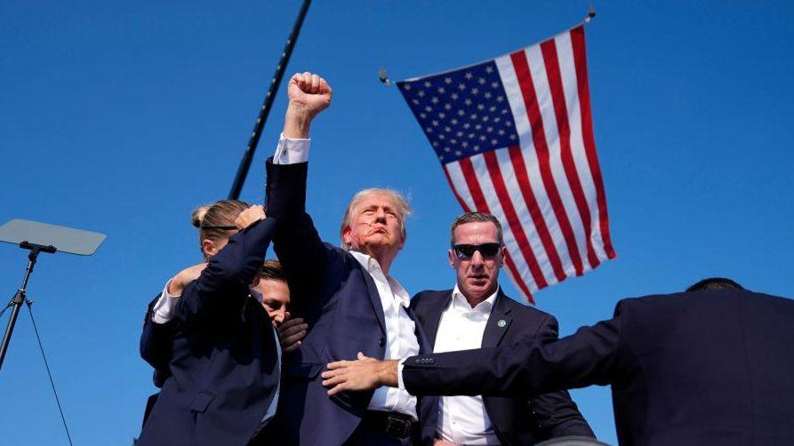 Donald Trump raises his fist as he is surrounded by US Secret Service agents after the shooting