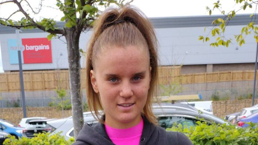 Holly Newton standing in a car park. She has long brown hair tied up in a ponytail and is smiling at the camera.